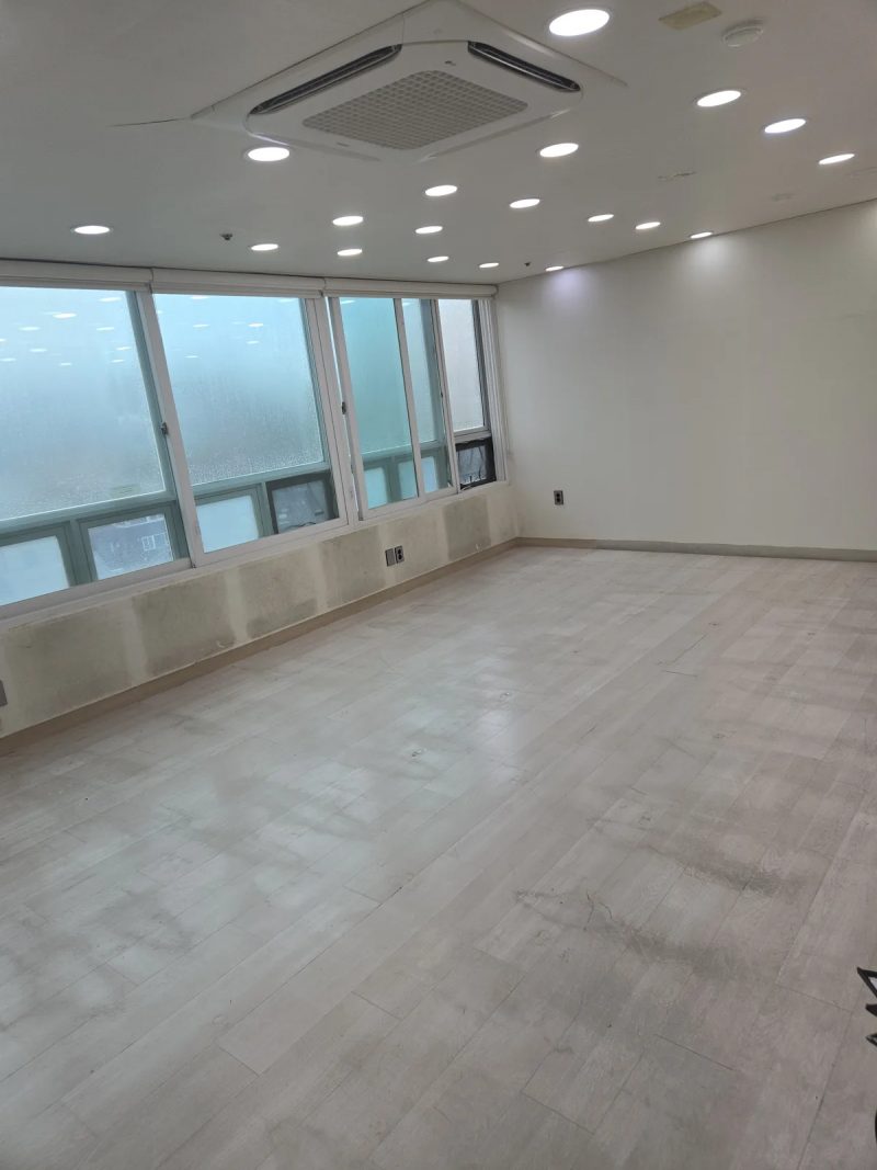천장에 시스템 냉방기가 설치된 넓은 빈 강의실, 방음재를 뗀 창가 벽면에 마감재 얼룩이 남아있는 모습