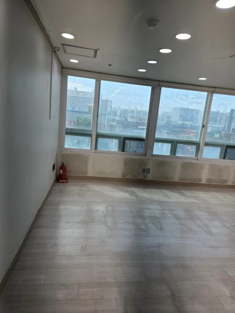 벽면 얼룩과 소화기가 보이는 빈 방, 창밖 도심 전경