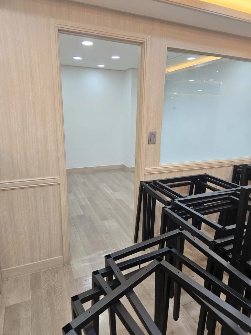 검정 철제 책상 다리 프레임이 바닥에 쌓이고 안쪽으로 빈 방이 이어지는 모습